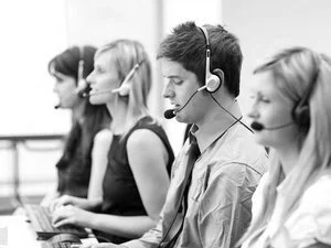A group of five customer service representatives with headsets sitting at desks in a call center, working on computers.