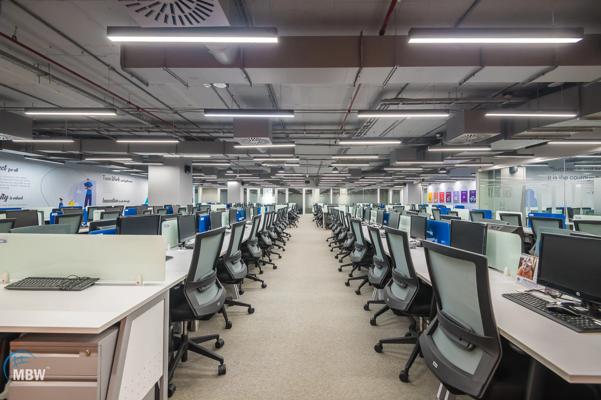 Empty office space with rows of desks and chairs, desktop computers, and motivational wall posters