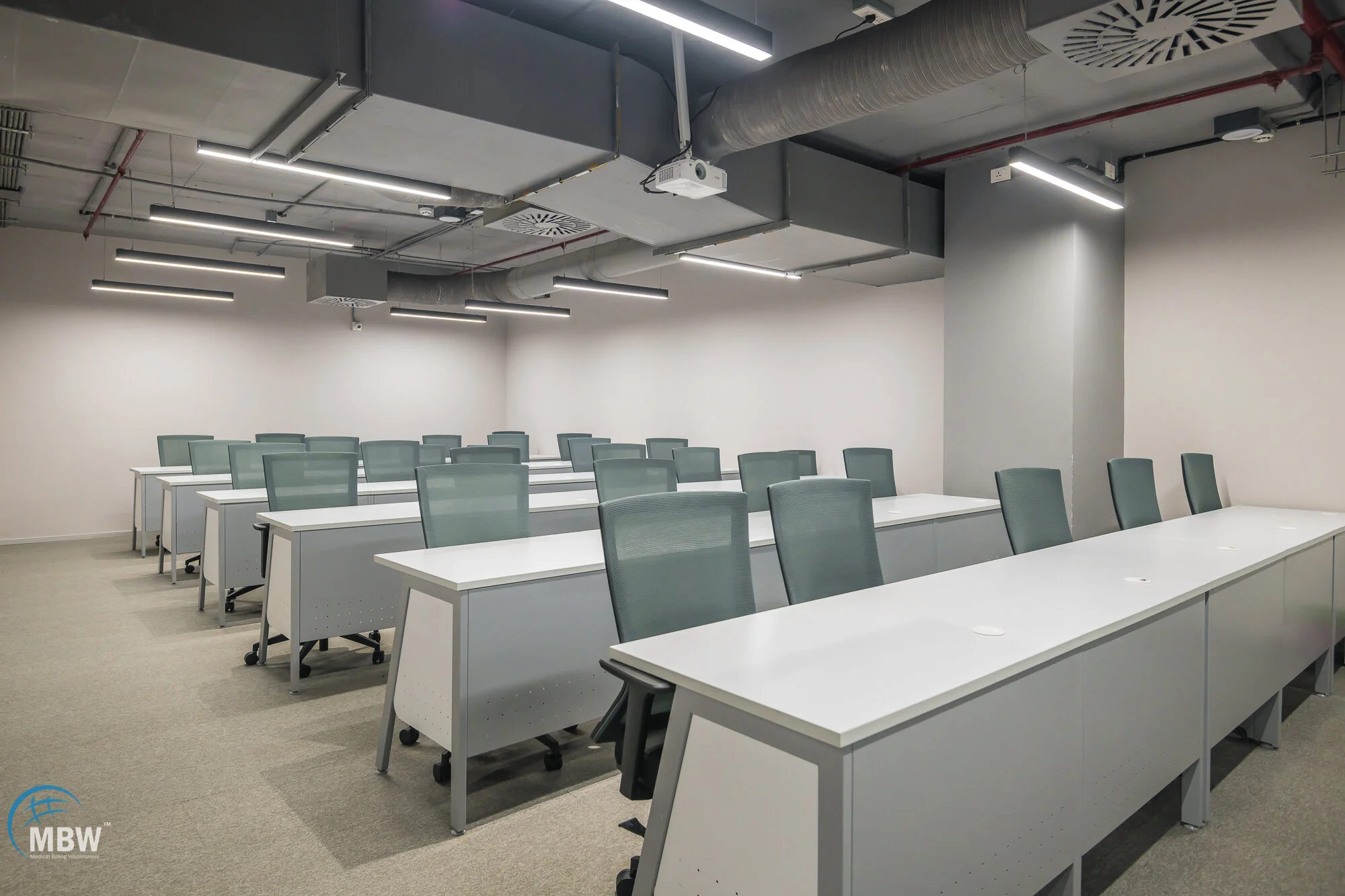 Empty modern conference room with white tables and green chairs, fluorescent lighting, exposed ductwork, white walls, and carpeted floor.