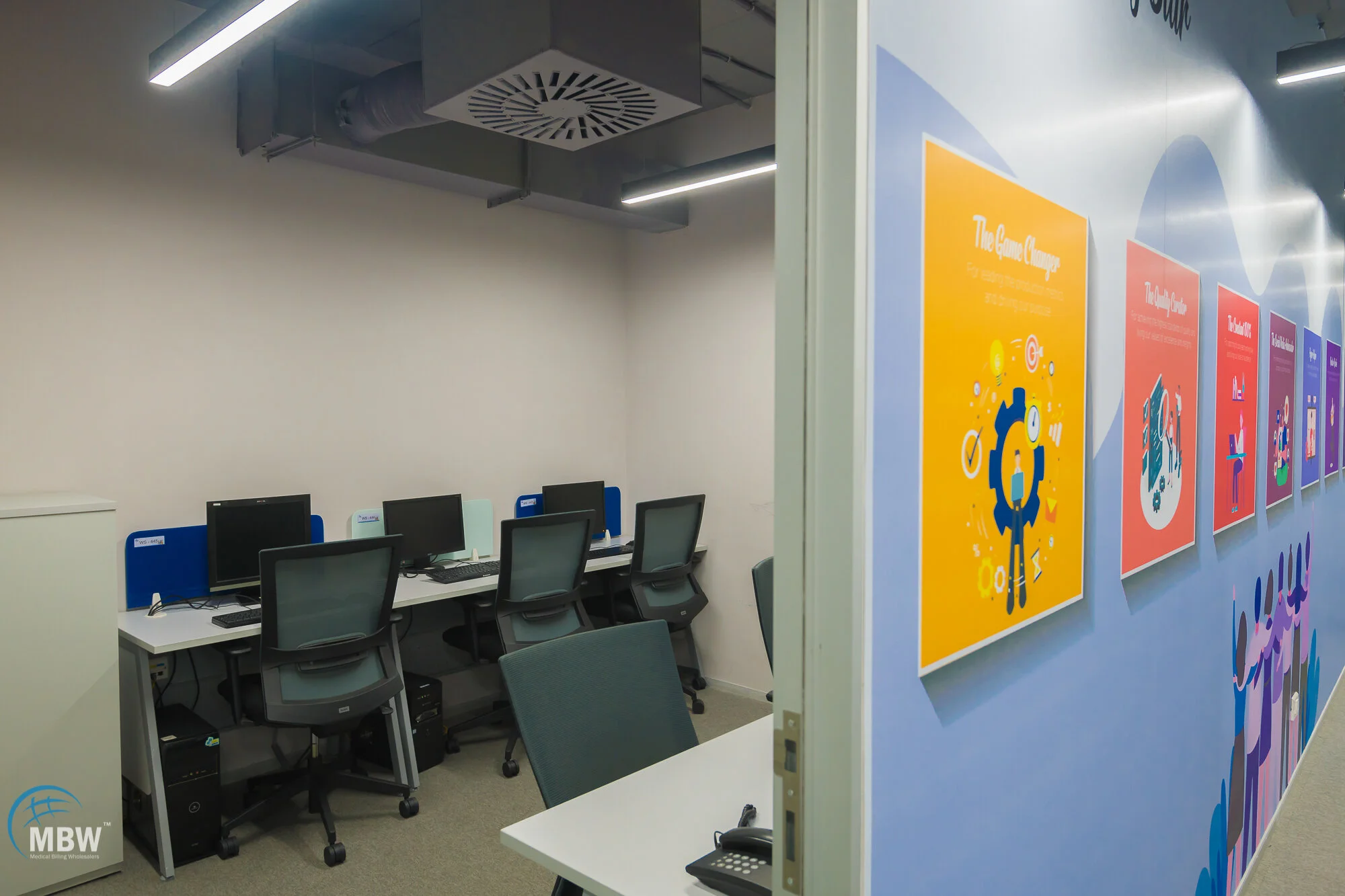 Office computer room with four computers and chairs, and colorful motivational posters on the hallway wall.