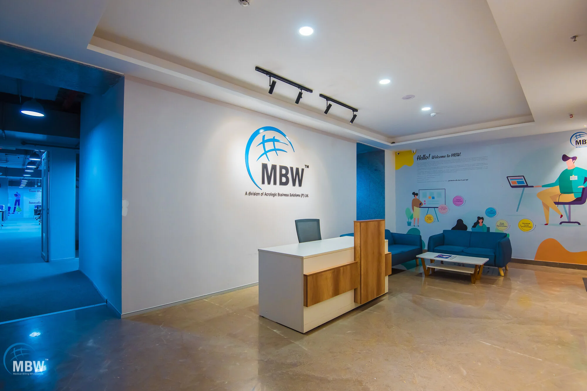Reception area with white wall displaying MBW logo and slogan, blue seating area, and colorful illustrations on the wall.