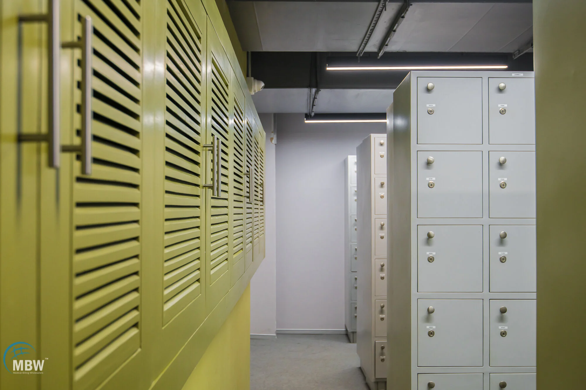 Row of gray lockers in a hallway with yellow cabinets on the left side.