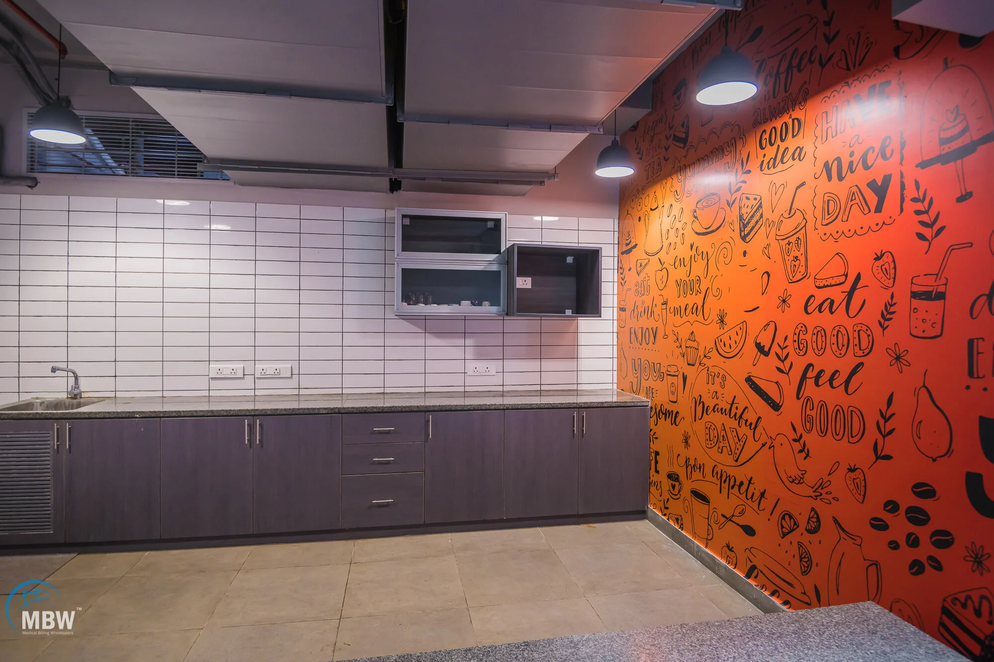 Empty kitchen with white tiled wall, dark wood cabinets, and an orange wall decorated with black doodles and motivational words.