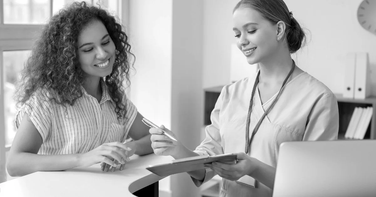 A nurse or healthcare professional assisting a smiling female patient, showing a friendly interaction in a medical office setting.